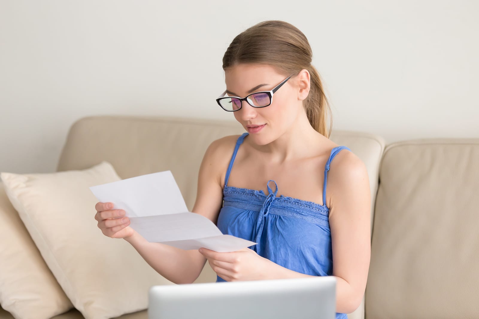 young woman holding letter sitting near laptop