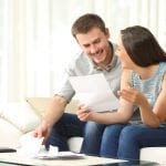 Happy couple reading mail and checking accountancy looking each other sitting on a couch at home