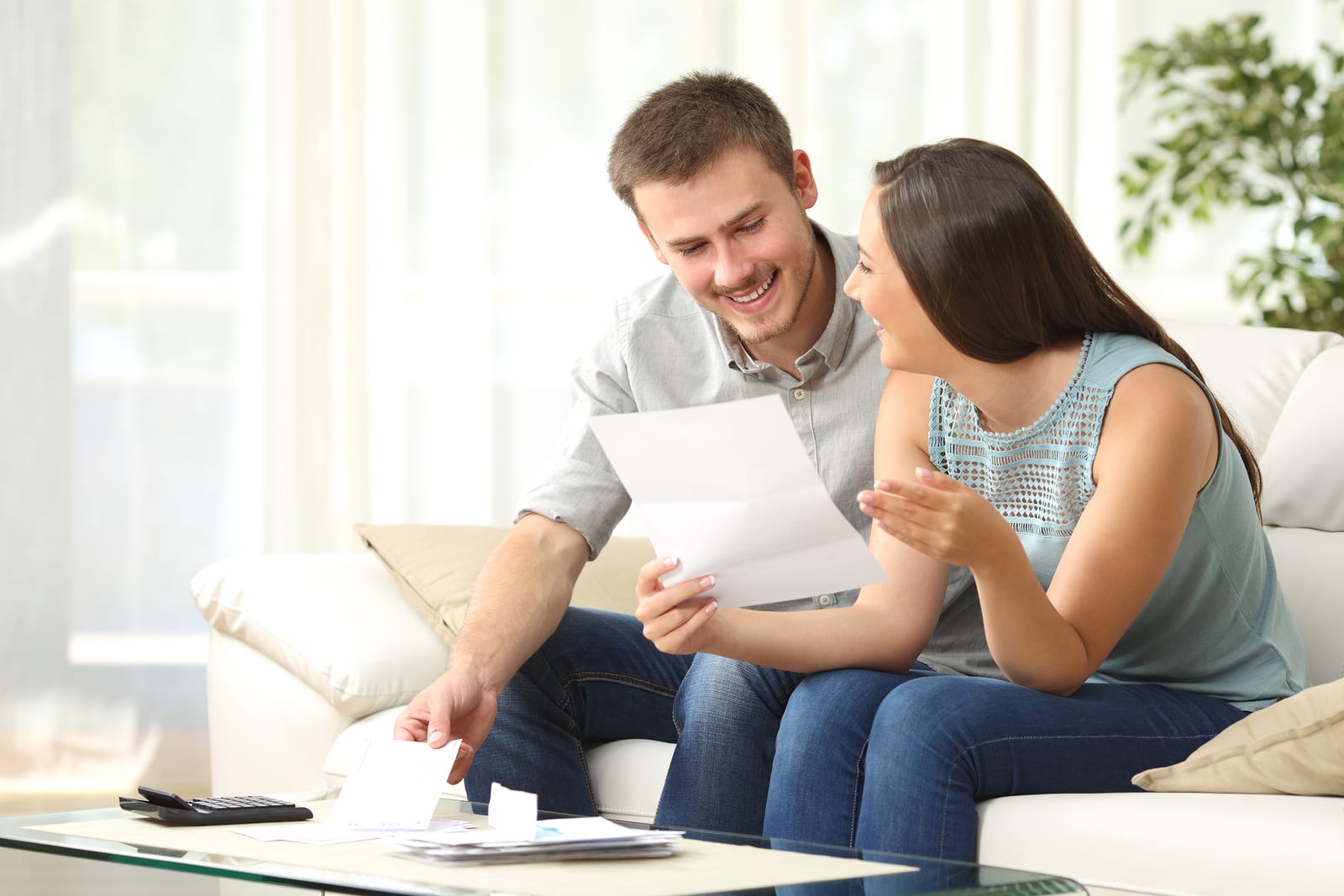 Happy couple reading mail and checking accountancy looking each other sitting on a couch at home