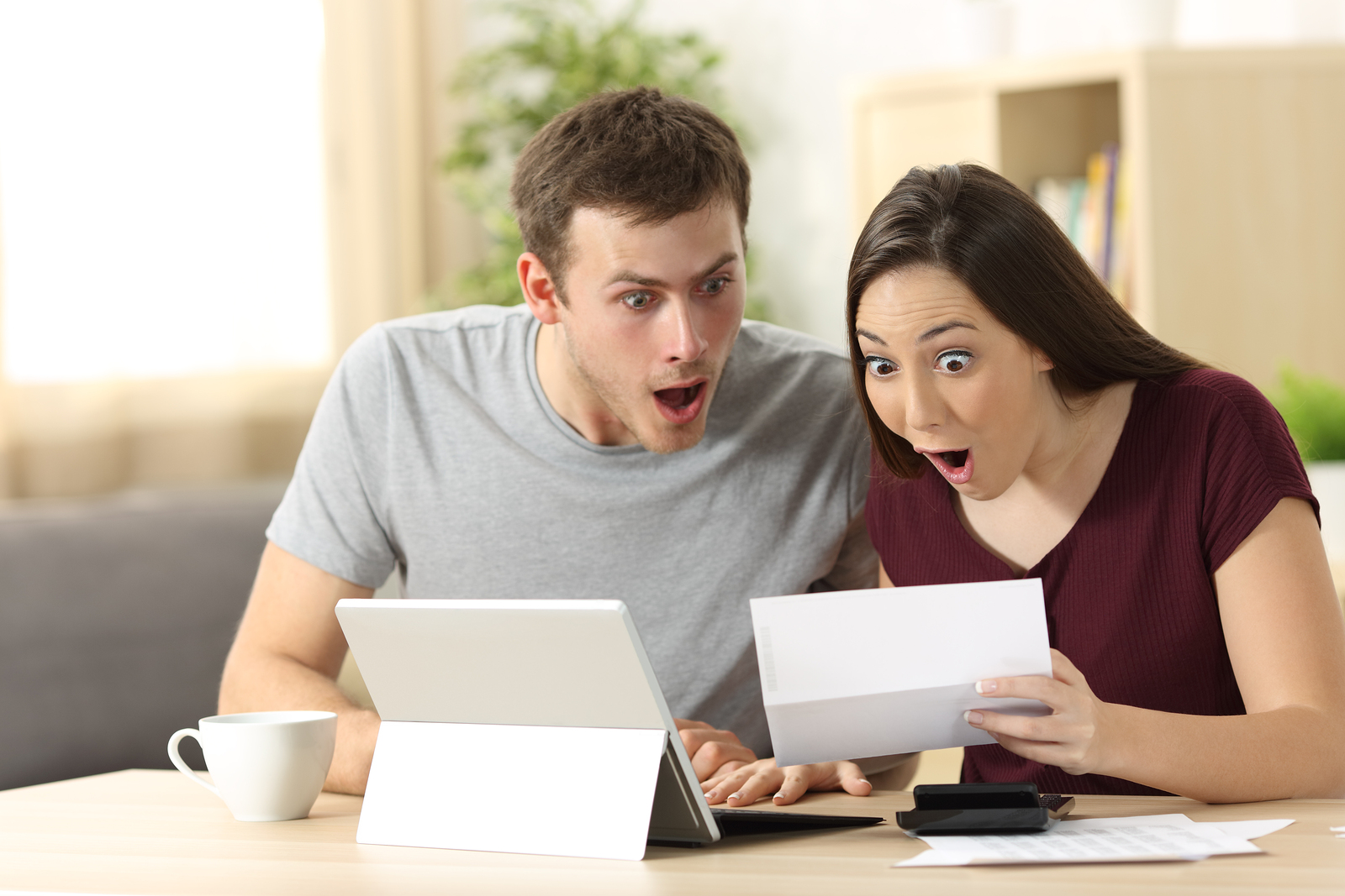 Amazed couple reading together a letter sitting in a desk at home