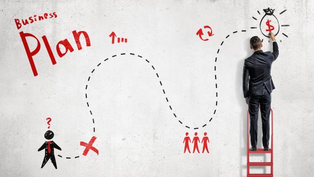 bigstock–210248173 A businessman draws a red and black simplified business plan as a map to success on a white wall. Business and success. Yearly plan. Setting big goals.