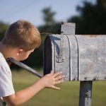 A cute boy, checking the mail in an open mail box. The kid is waiting for the letter, checks the correspondence and looks into the metal mailbox.