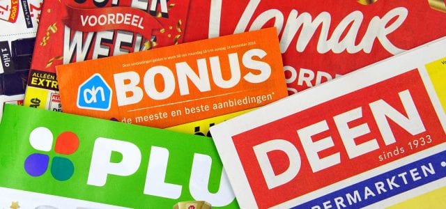 Amsterdam, the Netherlands - December 9, 2018: Stack of grocery shop sale flyers or advertising brochures, of Dutch supermarkets against a wooden background.