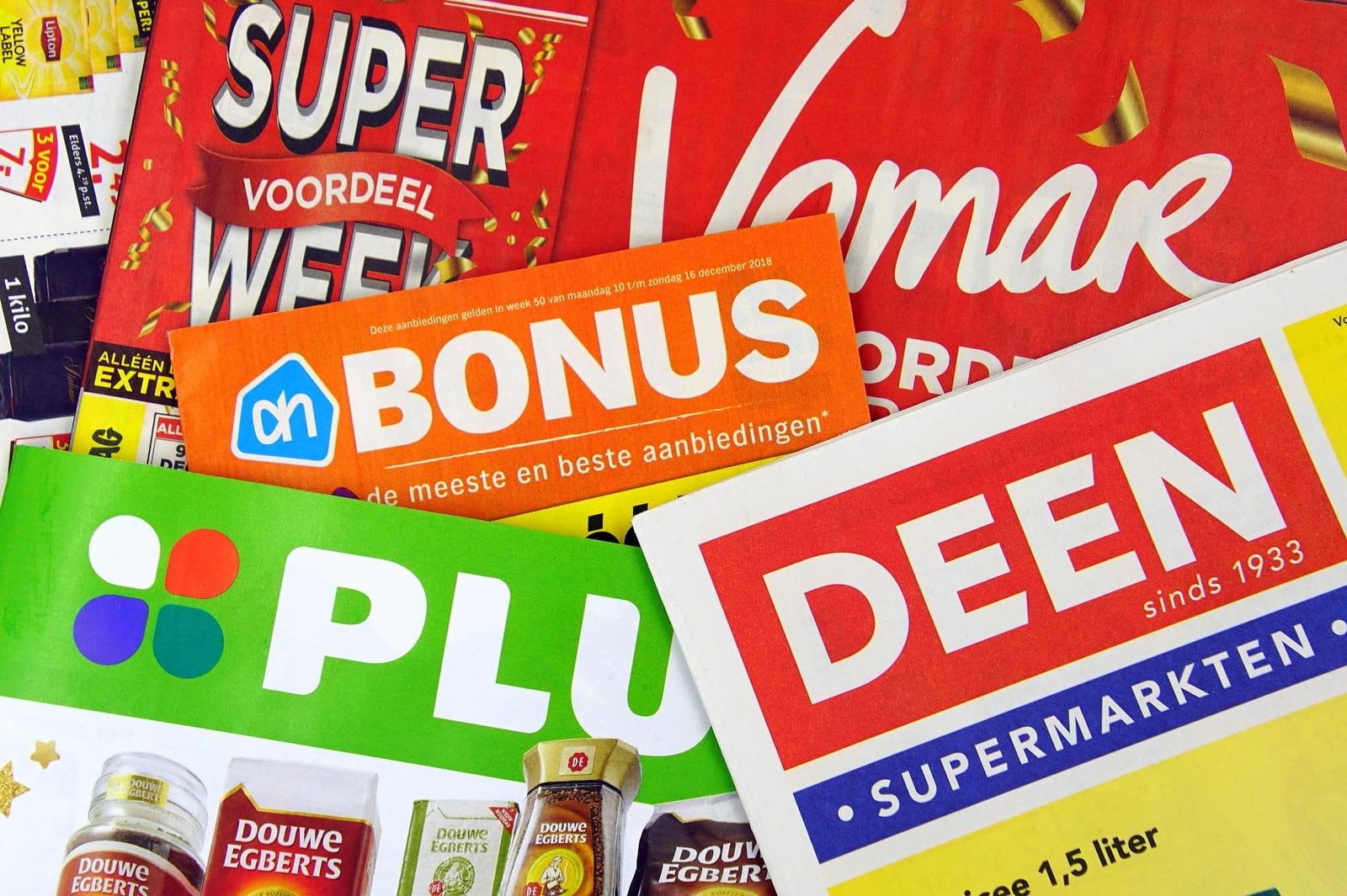 Amsterdam, the Netherlands - December 9, 2018: Stack of grocery shop sale flyers or advertising brochures, of Dutch supermarkets against a wooden background.