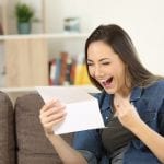 Excited woman reading great news in a letter sitting on a couch in the living room at home