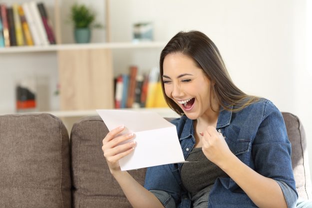 Excited Woman Reading Great News In A Letter Sitting On A Couch Excited woman reading great news in a letter sitting on a couch in the living room at home
