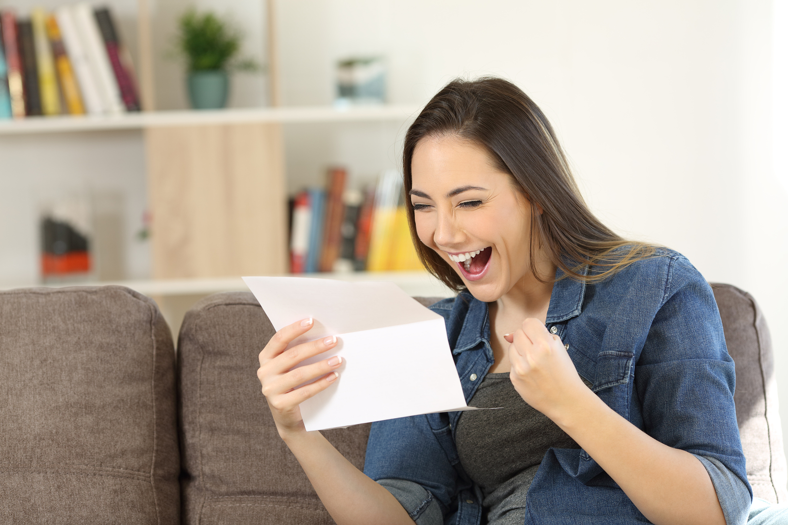 Excited woman reading great news in a letter sitting on a couch in the living room at home