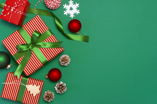 Gift Boxes, Christmas Balls, Toys, Fir Cones, Ribbon On Green Ba Gift boxes, Christmas balls, toys, fir cones, ribbon on green background. Festive, congratulation, New Year Christmas presents Xmas holiday 2019 greeting card. Flat lay, top view, copy space.