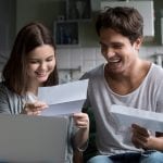 Happy young couple excited by reading good news in paper letter about refund tax money, millennial man and woman glad to receive special offer about cheap deal, direct mail, test results or invitation by mail