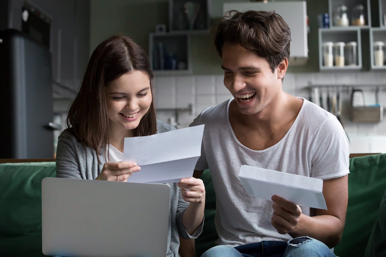 Happy young couple excited by reading good news in paper letter about refund tax money, millennial man and woman glad to receive special offer about cheap deal, direct mail, test results or invitation by mail