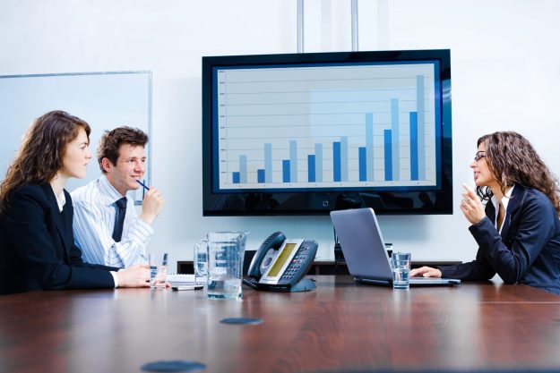 Happy young businesspeople having meeting in boardroom at office Small business employees discuss strategies that larger businesses utilize and how they can be applied on a smaller scale.