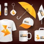 A t-shirt, mug, bag, hat, umbrella, flag, and office supplies all display custom orange logos to promote a business.