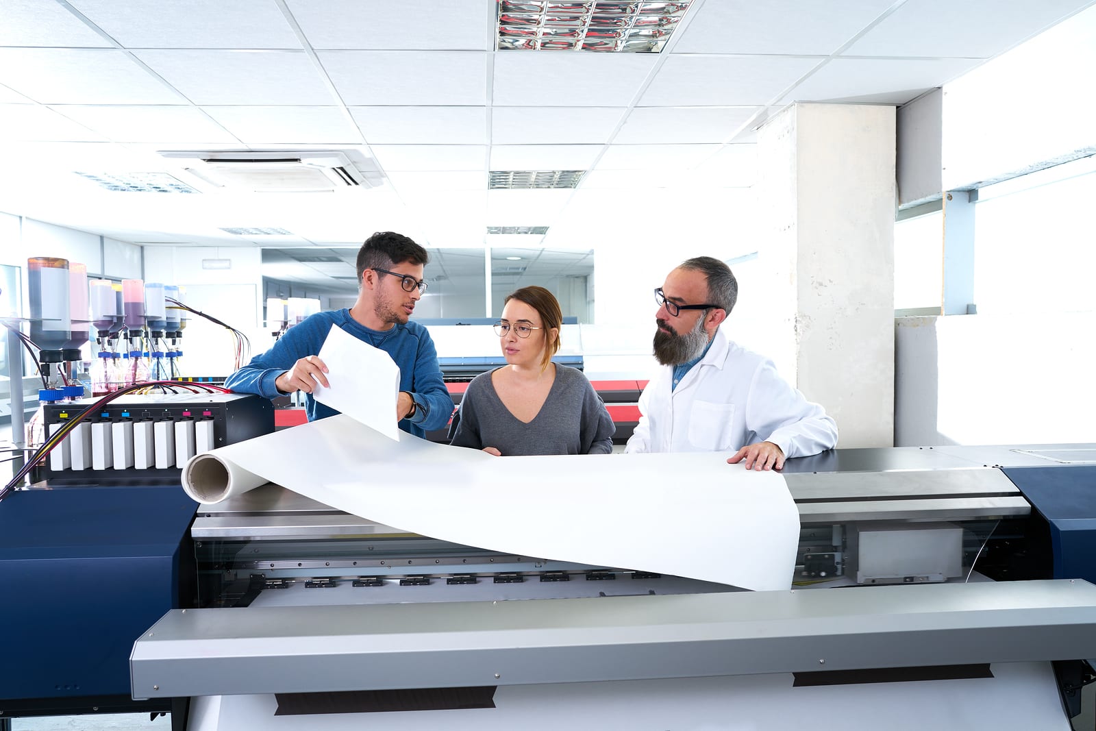 A team of two men and a woman work to isolate a problem with a design in a printing facility.