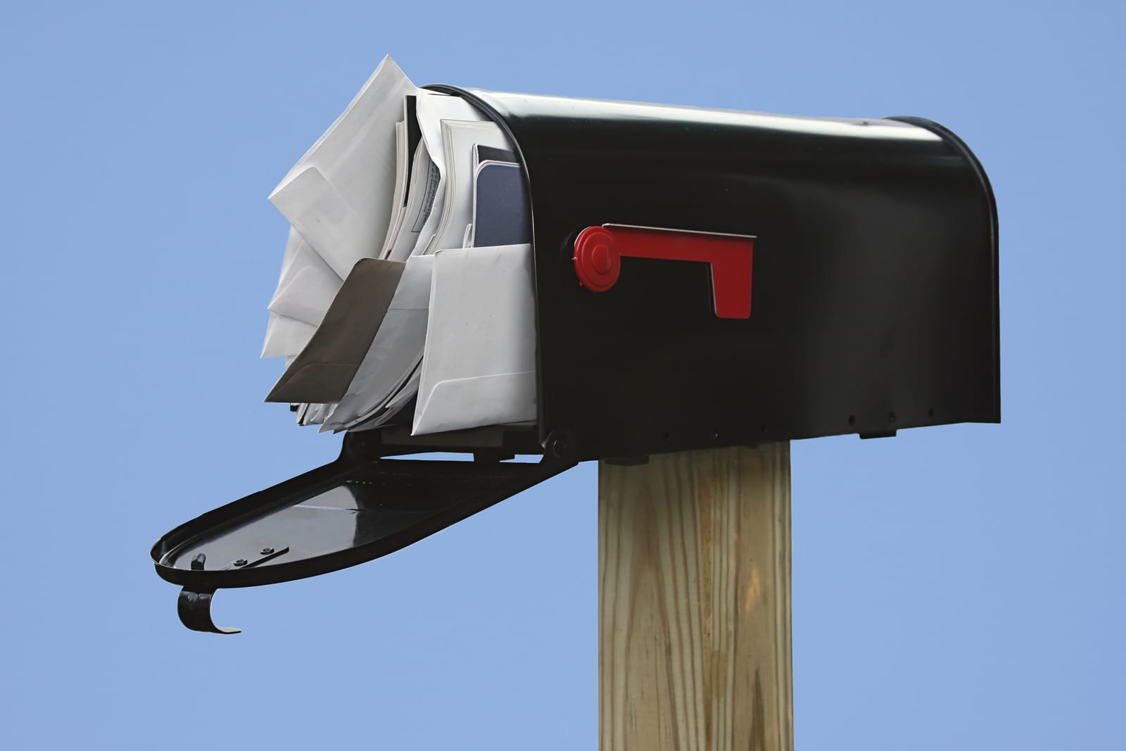 Black Mailbox stuffed with junk mail on a blue background