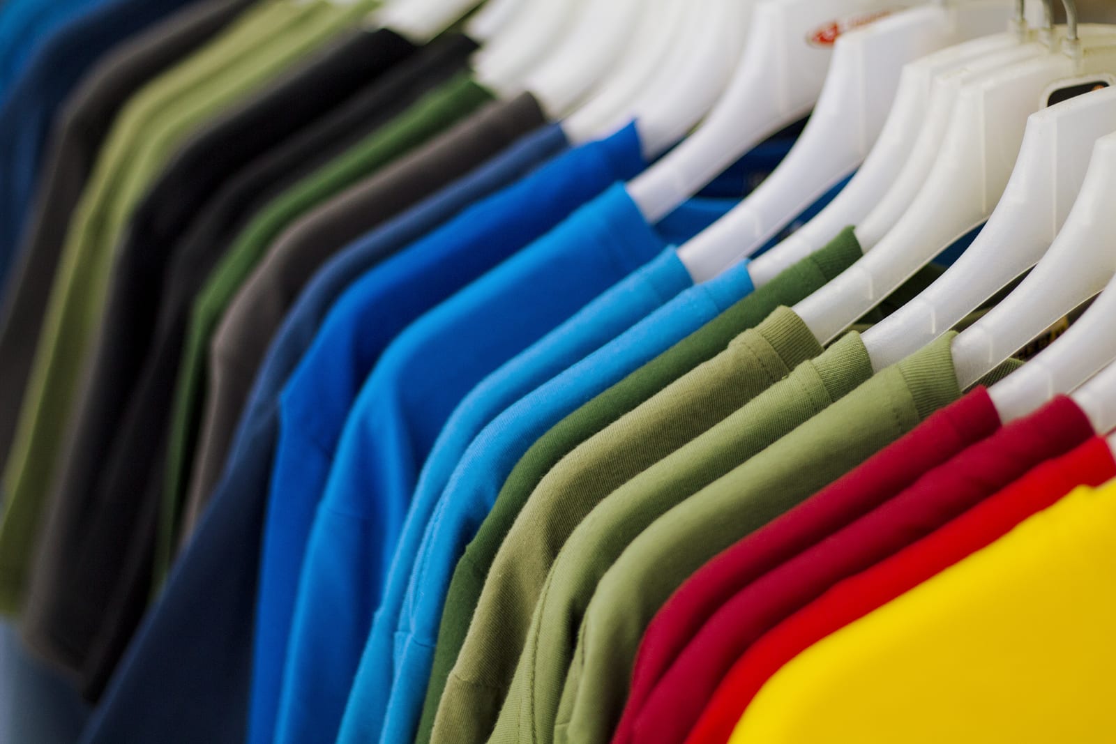 Promo Items Colorful t-shirts on hang for sale in shop. Multicolored summer top on hanger. Summer season clothes department store. Unisex apparel for warm weather. Summer sale in shopping mall. Rainbow tshirts